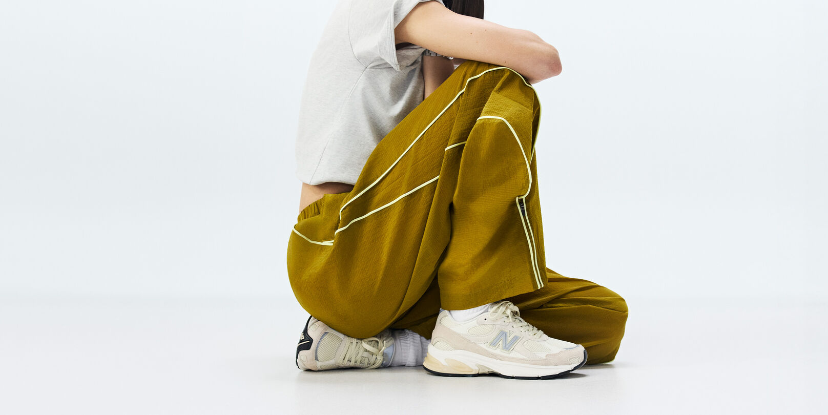 Knee-down of a woman sitting wearing New Balance sneakers on a white background